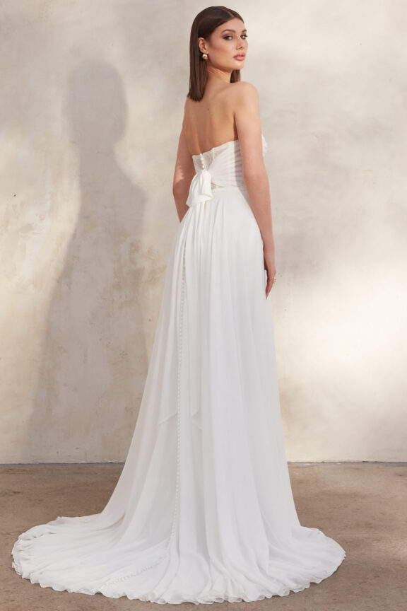 Strapless trouwjurk van Justin Alexander met een elegant geplooid lijfje en een zachte chiffon rok, afgewerkt met een speelse strik aan de achterzijde en een subtiele sleep.