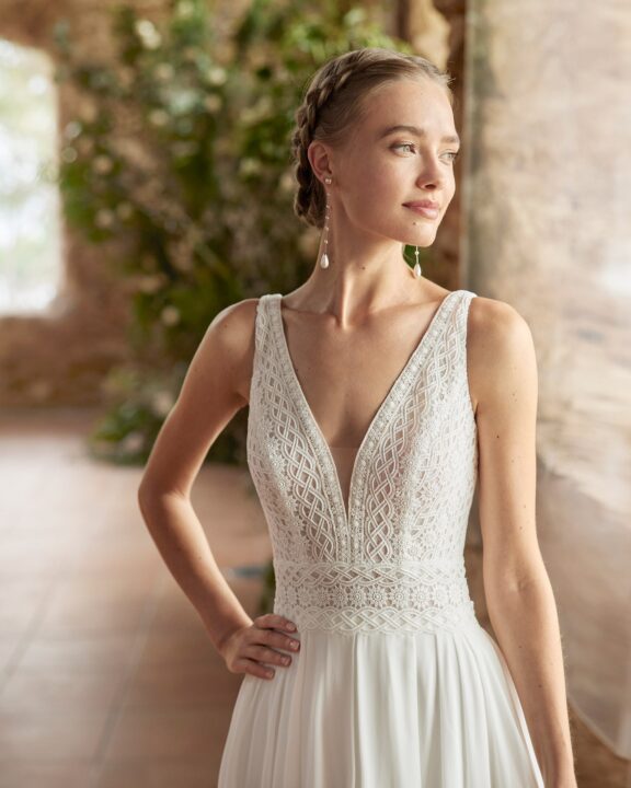 Boho trouwjurk met een diepe V-hals, kanten details en een elegante split, ontworpen door Alma Novia - Rosa Clará. Perfect voor een romantische bruiloft.