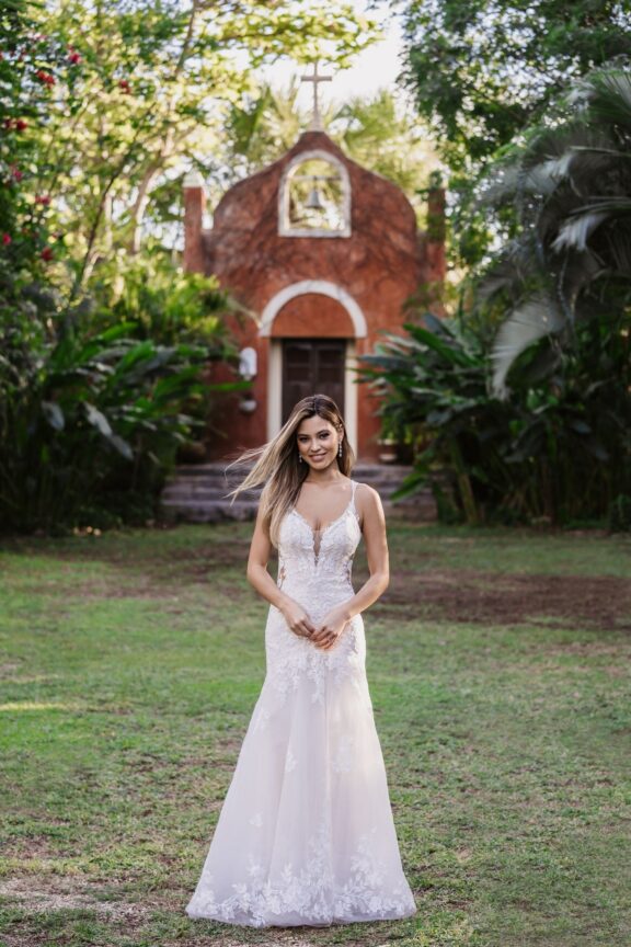 Elegante trouwjurk van het merk Allure Bridals, met een aansluitend silhouet, delicate kanten details en een dramatische sleep. De jurk heeft dubbele bandjes en een transparante rug met kanten motieven, perfect voor een romantische bruiloft in de natuur.