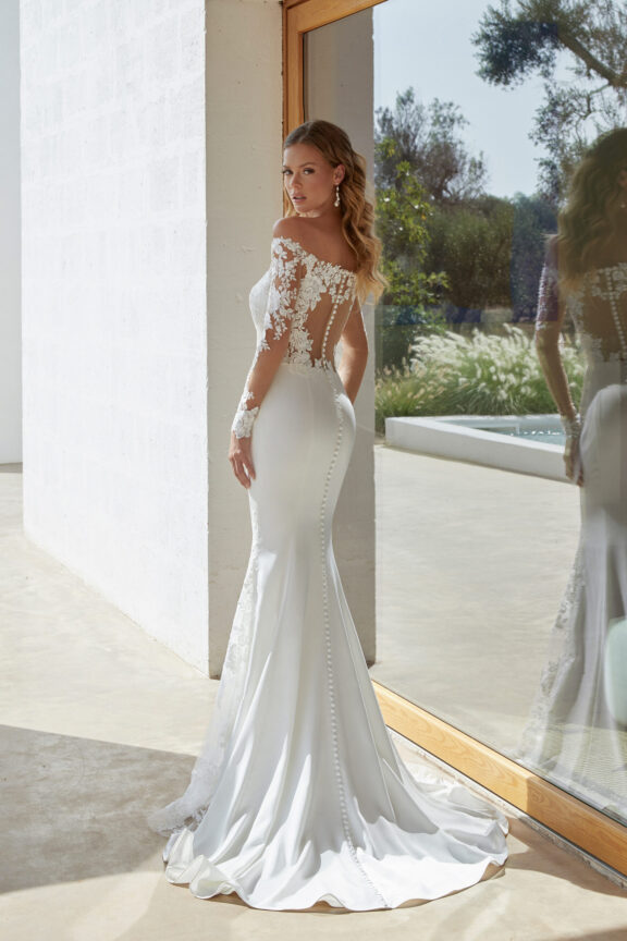 Elegante trouwjurk van Justin Alexander - Adore, met off-shoulder bloemenkant, lange mouwen en een aansluitend silhouet. Perfect voor een tijdloze en verfijnde bruid.